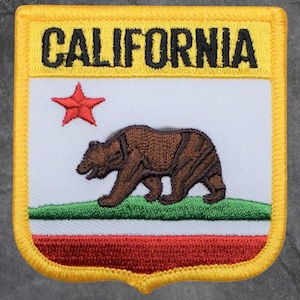 Peut inclure: Écusson brodé avec le mot "CALIFORNIA" en noir sur un bord jaune. L'écusson représente le drapeau de l'État de Californie avec un ours brun, une étoile rouge et des rayures rouges, blanches et vertes.