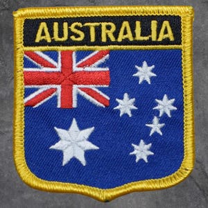 May include: Embroidered patch featuring the Australian flag. The patch has a blue background with the Union Jack in the upper left corner and white stars. The word "AUSTRALIA" is embroidered in yellow letters on a black background.