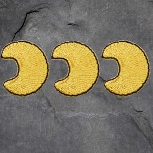 May include: Three embroidered yellow crescent moon patches with a dark brown border. The patches are arranged horizontally against a gray, textured background.