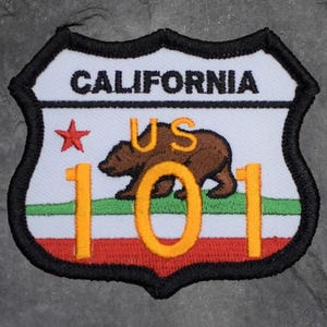 May include: Embroidered patch featuring the word "CALIFORNIA" above a brown bear and the text "US 101". The patch has a white background with a red star and green and red stripes at the bottom. The border is black.