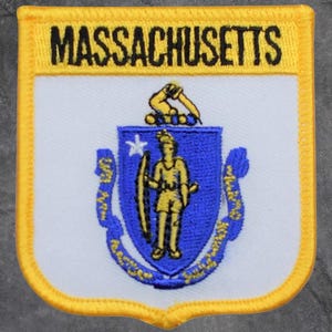 May include: A rectangular patch featuring the Massachusetts state seal. The patch has a white background with a blue shield in the center. The shield contains a Native American figure and a star. The word "MASSACHUSETTS" is displayed in black letters on a yellow banner.