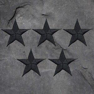 May include: Five black stars are carved into a dark gray stone surface.