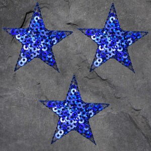May include: Three blue star-shaped patches made of sequins. The stars are on a gray background.