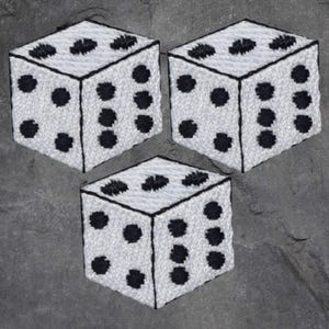 以下が含まれることがあります： 黒い点のある白いサイコロが3つあり、それぞれ異なる数字を示しています。サイコロは刺繍されており、表面にテクスチャがあります。