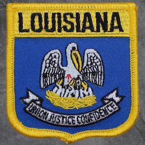 May include: Embroidered patch with the word "LOUISIANA" in black above a blue background. The patch shows a white pelican with a yellow beak and a red dot on its chest. The banner below reads "UNION JUSTICE CONFIDENCE". The patch has a yellow border.