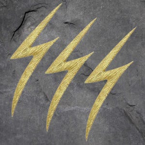 May include: Three gold lightning bolt symbols are carved into a dark gray stone surface.