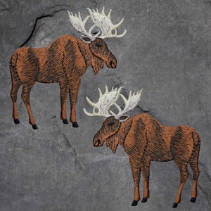 May include: Two embroidered moose on a gray background. The moose are brown with white antlers and black hooves. The embroidery has a textured appearance, and the background has a stone-like texture.