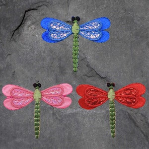 May include: Three embroidered dragonfly appliques in different colours: blue, pink and red. Each dragonfly has a green body and clear wings with a sparkly finish.