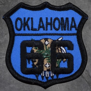 May include: A blue and black embroidered patch featuring the word "OKLAHOMA" at the top. The number "66" is in the center, with a Native American design. The patch has a black border.