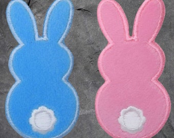 May include: Two felt bunny shapes, one blue and one pink, with white tails. The bunnies are in the shape of a traditional Easter bunny.