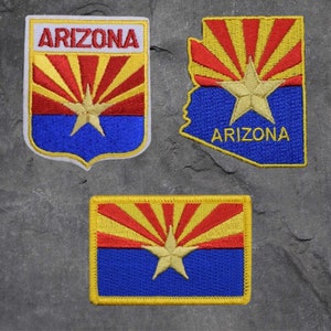 May include: Three embroidered patches featuring the Arizona state flag. The patches are yellow, red, and blue with a star in the center. The text "Arizona" is embroidered on two of the patches.