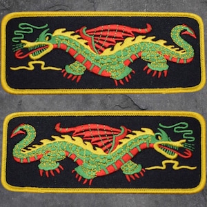 May include: Two embroidered patches featuring a green dragon with red and yellow accents. The dragon is depicted with wings and a long tail. The patches are rectangular and have a yellow border.