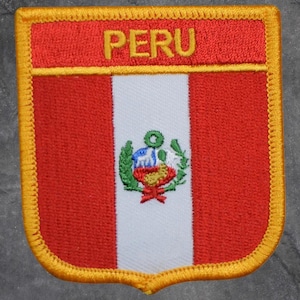 May include: Embroidered patch featuring the Peruvian flag. The design includes a red and white striped background with the Peruvian coat of arms. The word "PERU" is embroidered in gold at the top, and the patch has a gold border.