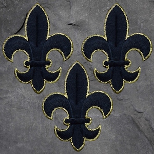 May include: Three navy blue fleur-de-lis patches with gold embroidered trim. The patches are arranged in a triangular pattern against a gray stone background. Each patch features a detailed design with a classic fleur-de-lis shape.