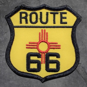 May include: Yellow and black Route 66 patch with the words "ROUTE 66" at the top. The patch features a red and black sun symbol in the center and the number "66" at the bottom. The patch has a black border.