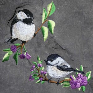 May include: Two embroidered black-capped chickadees perched on branches with purple flowers. The birds are white with black heads and wings.