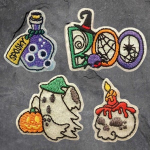 May include: Four embroidered iron-on patches with a Halloween theme. The patches feature a spooky potion bottle, a ghost holding a pumpkin, a skull with a candle, and a "BOO" with a spider web and spider.