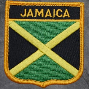 May include: Embroidered patch featuring the Jamaican flag design. The patch has a black and green background with a yellow diagonal cross. The word "JAMAICA" is embroidered in yellow at the top, with a gold border.
