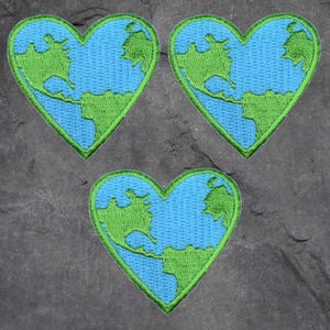 May include: Three heart-shaped patches with a blue and green Earth design. The patches have a blue background with green continents and a green border. The patches are embroidered.