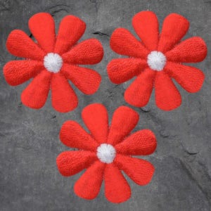 May include: Three red flower patches with white centers are arranged on a gray background. The flowers have textured petals, and the white centers provide a contrasting focal point. These patches could be used for clothing or craft projects.