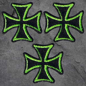 May include: Three black iron crosses with a green outline. The crosses are embroidered and have a textured fabric surface.