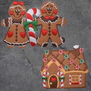 Peut inclure: Écussons de Noël brodés représentant un couple de pain d'épices tenant un sucre d'orge et une maison en pain d'épices. Les personnages en pain d'épices ont des cœurs rouges et la maison est décorée de bonbons. Les écussons sont marron, rouge, blanc et vert.