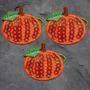 May include: Three orange pumpkin-shaped fabric patches with green leaves and red sequins. The patches are perfect for adding a festive touch to crafts and projects.
