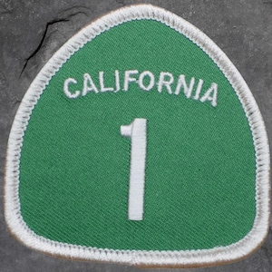 May include: A green and white patch featuring the text "CALIFORNIA" above the number "1". The patch has a white border and a green background. The patch is in the shape of a triangle.