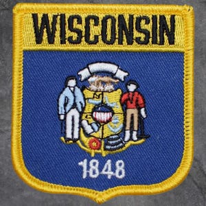 May include: Embroidered patch with the word "WISCONSIN" in black on a yellow banner. The patch has a blue background with the state seal and the year "1848" in white. The patch has a yellow border.