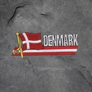 Könnte beinhalten: Ein Aufnäher mit der dänischen Flagge, einem weißen Kreuz auf rotem Grund, und dem Wort "DENMARK" in silbernen Buchstaben. Die Flagge befindet sich auf einer rot-weiß gestreiften Basis mit einer goldenen Stange.