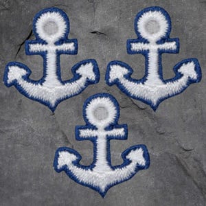 以下が含まれることがあります： 3つの刺繍されたアンカーパッチ。各パッチは、青いアウトラインの白いアンカーデザインが特徴です。アンカーは、グレーのテクスチャード加工された背景に配置されています。航海をテーマにした工芸品やアパレルに適しています。
