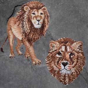 May include: Two embroidered lion patches. The first patch is a full-body lion with a brown mane and a light brown body. The second patch is a lion's head with a brown mane and a light brown face.