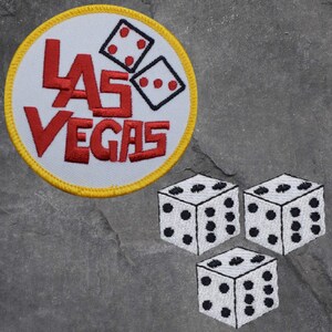 May include: A white embroidered patch with the words "Las Vegas" in red and yellow stitching. Three white dice with black dots are embroidered on a gray background.