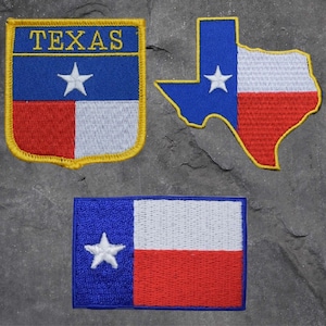 May include: Three embroidered patches featuring the Texas state flag. The first patch is a shield shape with the words "TEXAS" in yellow lettering above a blue and red flag with a white star. The second patch is a blue and red outline of the state of Texas with a white star. The third patch is a rectangular blue and red flag with a white star.