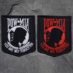 Könnte beinhalten: Zwei schwarze gestickte Patches mit den Worten "POW-MIA" und "You Are Not Forgotten" in weißer und roter Schrift. Die Patches zeigen eine Silhouette eines Soldatenkopfes in einem Kreis.