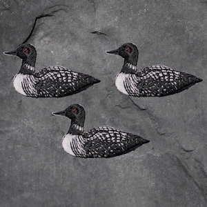 Könnte beinhalten: Drei schwarze und weiße Seeadler-Aufnäher mit roten Augen. Die Aufnäher sind gestickt und haben einen weißen Umriss.