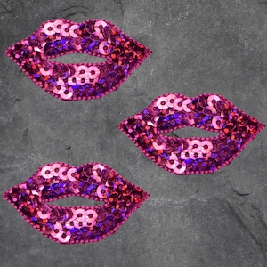 May include: Three pink sequined lips patches. Each patch is made of pink sequins with a purple iridescent sheen.