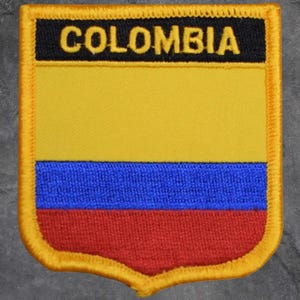 Peut inclure: Écusson brodé représentant le drapeau de la Colombie. Le patch présente un design jaune, bleu et rouge, avec le mot "COLOMBIA" en lettres jaunes sur fond noir. Le patch a une bordure dorée.