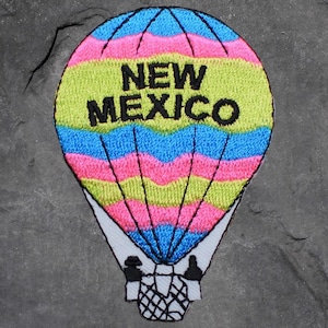 Peut inclure: Écusson brodé en forme de montgolfière avec des rayures bleues, roses et jaune-vert. Le texte "NEW MEXICO" est brodé en noir au centre du ballon. Le patch a une bordure blanche.