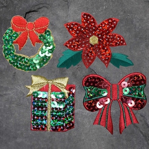 May include: Four Christmas-themed iron-on patches with a green and red color scheme. The patches feature a wreath, a poinsettia, a bow, and a gift box.