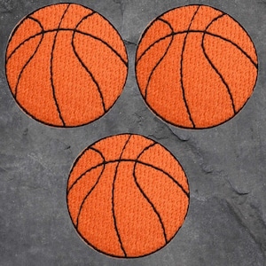 Könnte beinhalten: Drei orangefarbene Basketball-Patches mit schwarzen Nahtdetails. Die Patches sind rund und weisen das klassische Basketball-Panel-Design auf. Die Patches sind in einem dreieckigen Muster auf einem dunkelgrauen Hintergrund angeordnet.