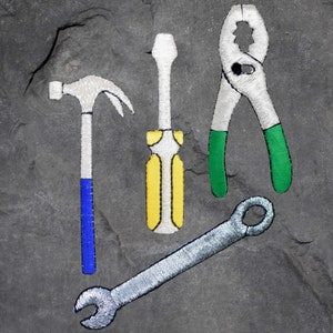May include: A set of four tools, including a hammer, screwdriver, pliers, and wrench, are embroidered on a grey stone background. The tools are white with yellow, blue, and green accents.