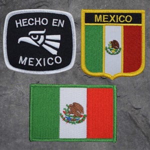 May include: Three embroidered patches with Mexican themes. One patch is black with white text and a white eagle design, reading "HECHO EN MEXICO". Another is a shield shape with the word "MEXICO" and the Mexican flag. The third is a rectangular Mexican flag.