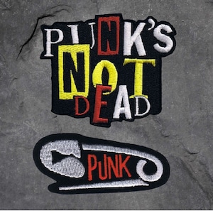 May include: Two embroidered patches. The first patch is black with white, red, and yellow lettering that reads "PINK'S NOT DEAD". The second patch is a black and white safety pin with the word "PUNK" in red lettering.