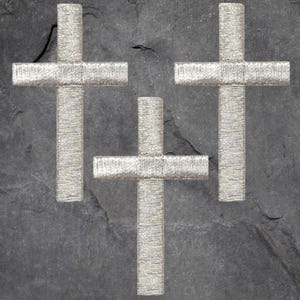 May include: Three silver crosses on a dark gray background. The crosses are made of a textured material and are arranged in a triangular pattern.