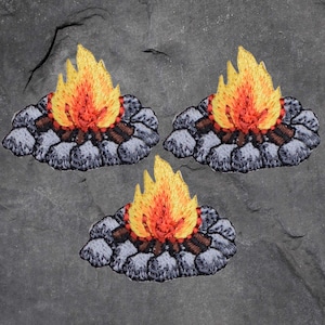 May include: Three embroidered patches with a campfire design. Each patch depicts a flame in yellow and orange hues above a pile of grey rocks and brown logs. The patches are designed for sewing or ironing onto fabric.