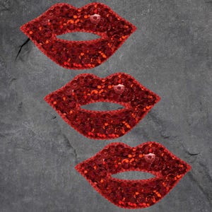 Könnte beinhalten: Drei rote Lippen-Patches aus Pailletten. Die Lippen sind rot umrandet und haben ein glänzendes, glitzerndes Finish.