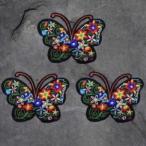 May include: Three black embroidered iron-on patches of colorful butterflies with floral designs.