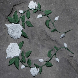 Könnte beinhalten: Weiße gestickte Rosen mit grünen Blättern und Stielen auf grauem Hintergrund.