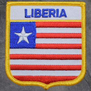 May include: Embroidered patch featuring the flag of Liberia. The patch has a white background with red and white stripes, a blue square with a white star, and the word "LIBERIA" in blue. The patch is bordered with yellow.